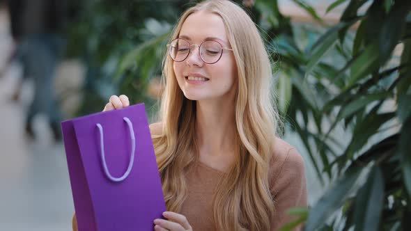 Portrait Excited Young Woman with Glasses Shakes Gift Bag Amazing Caucasian Millennial Birthday Girl
