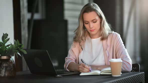 Smiling Freelancer Woman Working Remotely at Outdoor Summer Cafe Taking Notes Use Laptop at Table