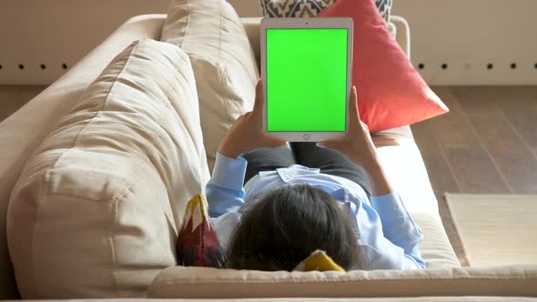 Top view of curly mixed race woman lying in bed at home using electronic tablet with green screen