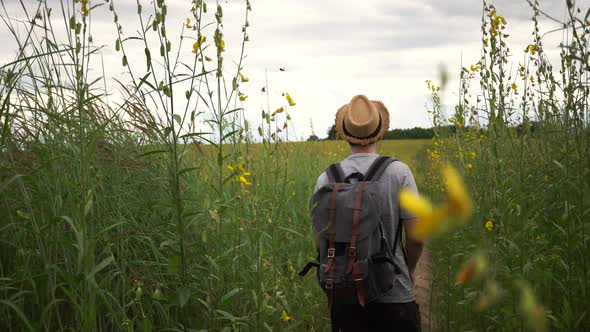 Young Male Tourist Backpacker with Hat and Bag Walking in the Countryside Grassland in Thailand