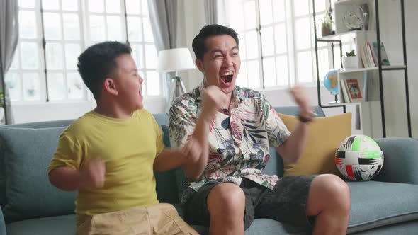 Asian Father And His Son Celebrating While Watching Tv At Home