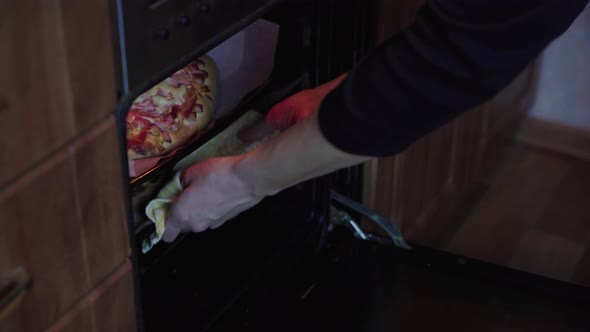 women's hands take baked pizza out of the oven