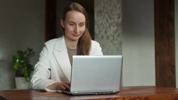 Portrait of a Young Business Woman in a White Jacket Looking Into the Camera Sitting at an Office