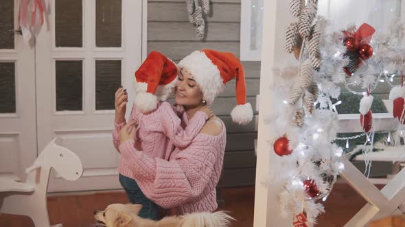 Young Mother and Daughter in Pink Pullovers and Red Hat Hugging at Christmas