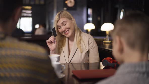 Portrait of Joyful Smiling Woman Bragging Credit Card Sitting with Husband and Son in Restaurant