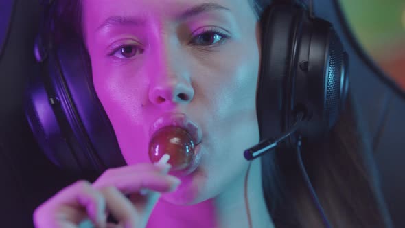 Girl with Plump Lips Gamer in Big Headphones in Gaming Club and Sucking a Lollipop