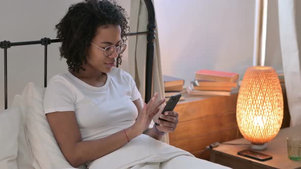 Smartphone Use By Young African Woman in Bed 