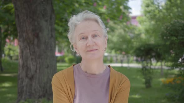 Portrait of Cute Old Woman with Grey Hair Smiling in the Green Amazing Park