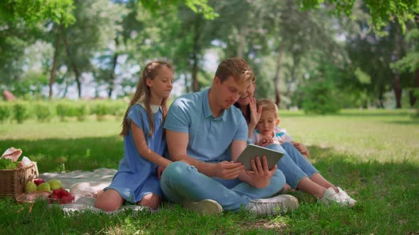 Young Family Sitting with Tablet on Sunny Park