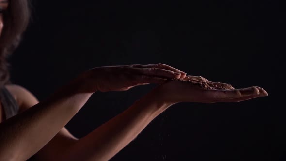 A Young Woman Hands the Falling Sand in Slow Motion on a Black Background. Slow Motion Studio.