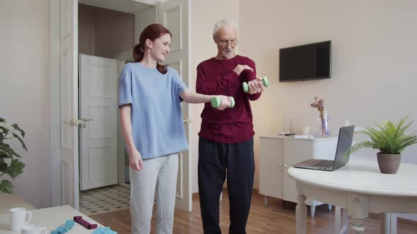 An Elderly Man and a Trainer Lift Dumbbells