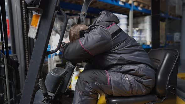 Side View Exhausted Overworked Caucasian Warehouse Loader Operator Sleeping Sitting in Forklift