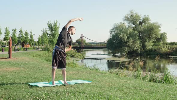 Athletic man stretching his muscles in morning in park. Fitness training activity.