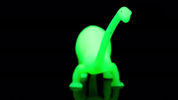 Green Toy Dinosaur Turning Agaisnt Black