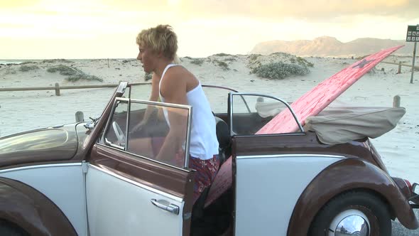 MS OF A YOUNG COUPLE GETTING OUT OF A CAR AND PICKING UP A SURFBOARD