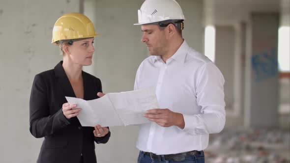 Two Architects Wearing Protective Helmet Works at Building Site