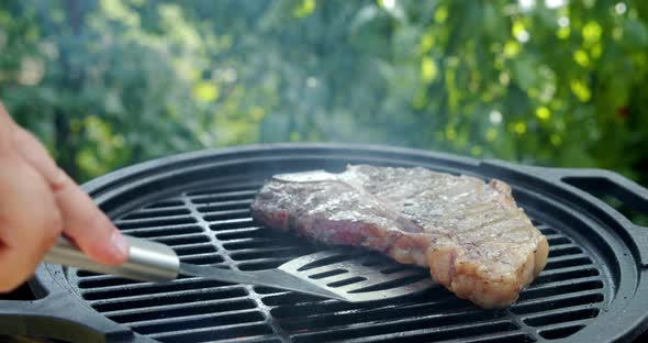 Steak T-bone Is Turned Over with a Spatula on Grill.