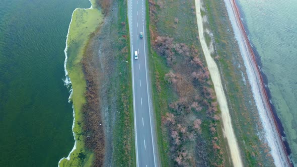 Aerial View of Two Cars Going Towards Each Other on a Dam Highway Surrounded By Lakes at Sunset