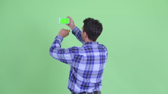 Rear View of Happy Young Hispanic Man Taking Picture with Phone