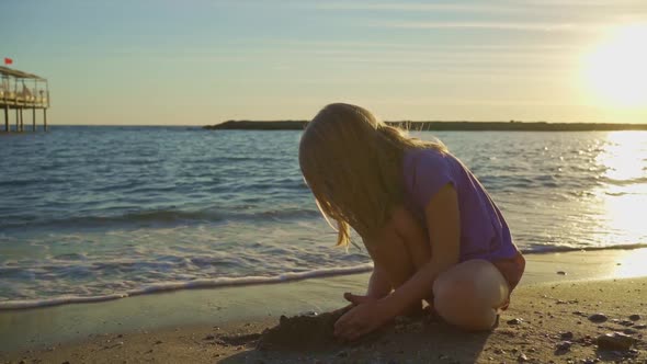 a Cute Little Girl Sits on the Seashore Playing in the Sand and with Pebbles