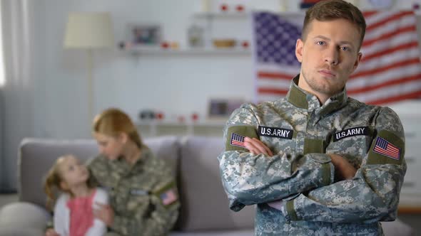 Serious American Soldier Looking at Camera Daughter and Military Wife Background