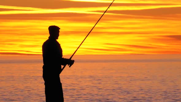 Silhouette of a Fisherman with a Fishing Rod at Sunset Over the Sea