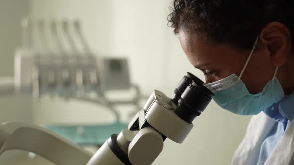 Masked Female Dentist Using Microscope During Work