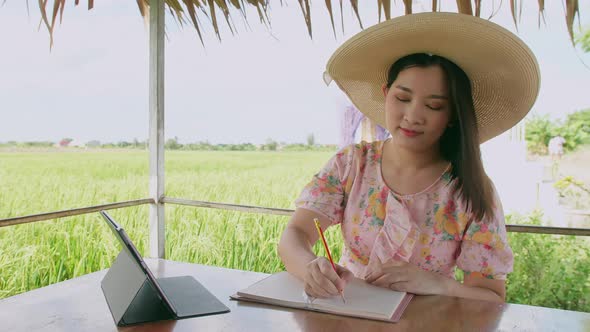 Freelance young woman working with her digital tablet outside her home. In the background rice plant