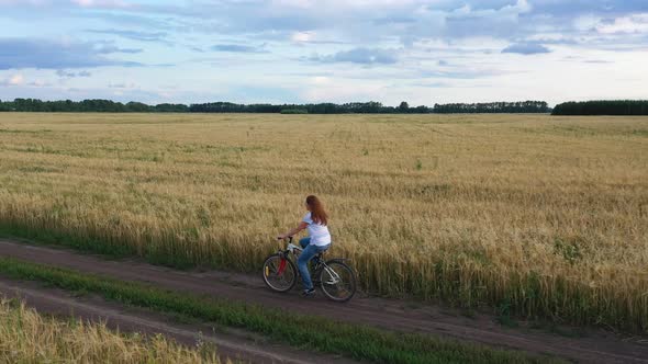 Girl with a Guy Riding a Bike Along a Wheat Field