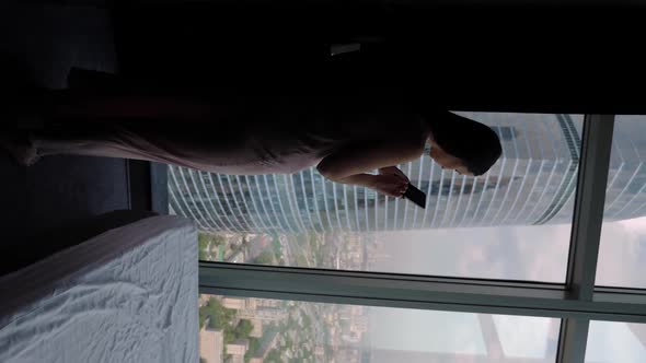 Woman in a Nightgown Approaches a Panoramic Window in a Skyscraper