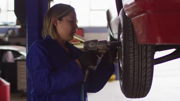 Female mechanic changing tires of the car using power drill at a car service station