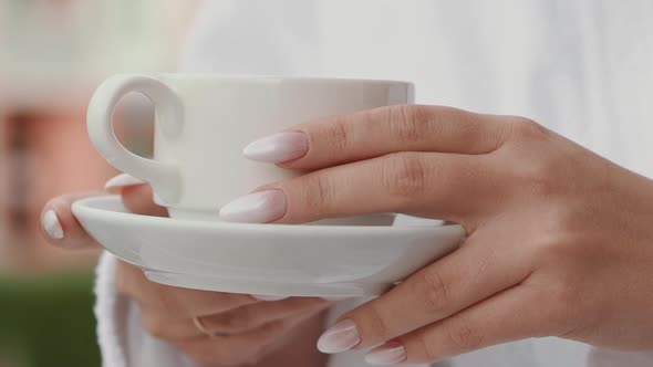 Lady with Elegant Manicure in Bathrobe Holds Cup of Coffee