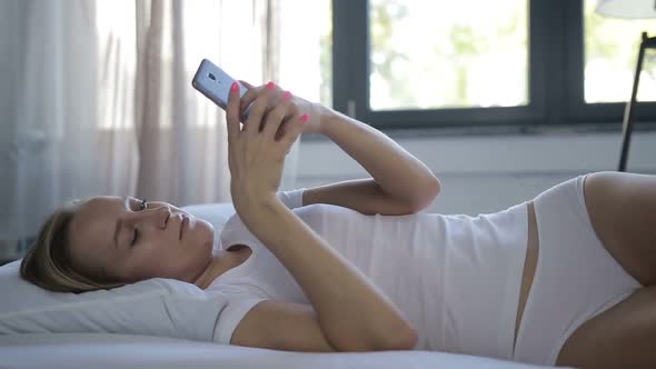 Woman in Bed Checking Social Apps with Smartphone
