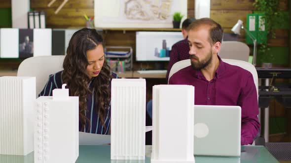 Team of Architects Taking Notes on Laptop with Building Models