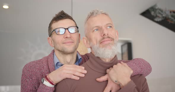 Happy Gay Couple Stands Hugging and Looking Outside Window