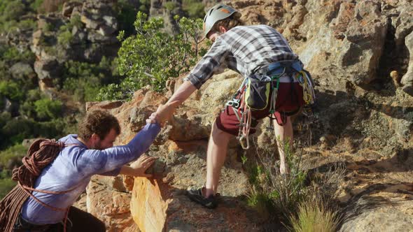 Man helping his friend to climb a cliff 4k