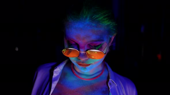 Portrait of Crazy Eccentric Woman in Darkness with Ultraviolet Light Makeup is Glowing in UV Flashes