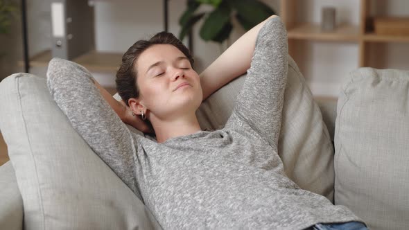 Serene Young Woman with Eyes Closed Put Hands Behind Head Relaxing on Cozy Soft Couch Taking Break