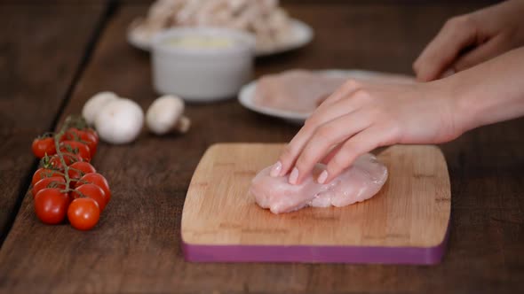 Female hands cutting chicken fillet on wooden chopping board.