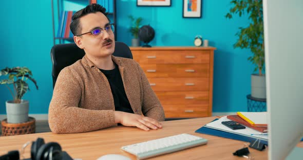 Man Wearing Glasses with Moustache is Sitting in Company Office in Front of Computer Screen