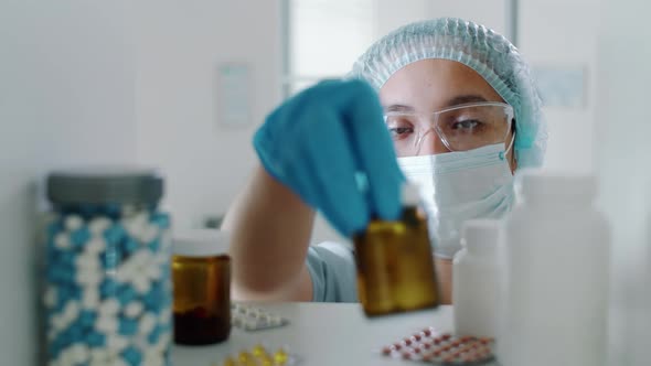 Nurse in Protective Uniform Taking Tablets from Shelf in Clinic