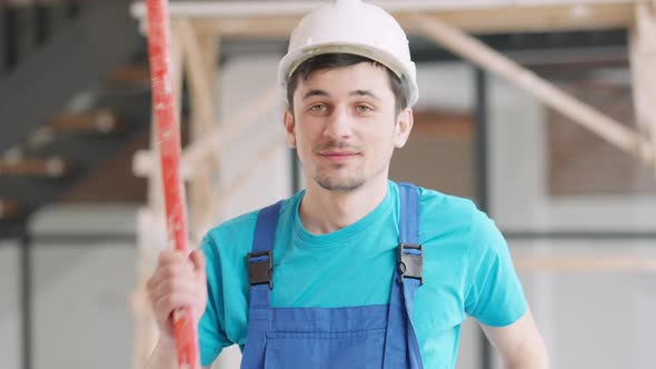 Positive Smiling Service Man in Hard Hat and Uniform Posing Indoors with Spirit Level