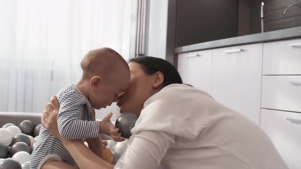 Asian Baby Playing in Ball Pit and Mom Kissing Him