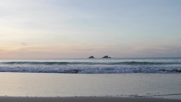 Ultra slow motion shot of waves breaking and swashing at sandy beach with beautiful colourful sky at