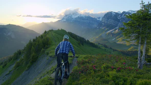 Mountain biker rides down an alpine ridge at sunrise