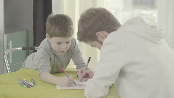 Father and Son Paint on Paper Sitting in Living Room at the Table