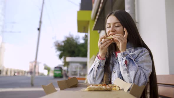 Portrait of a young woman eating pizza outdoors in the street