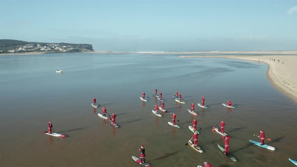 People Dressed In Santa Claus Doing Stand Up Paddle Boarding On Tranquil Water Of Obidos Lagoon Near