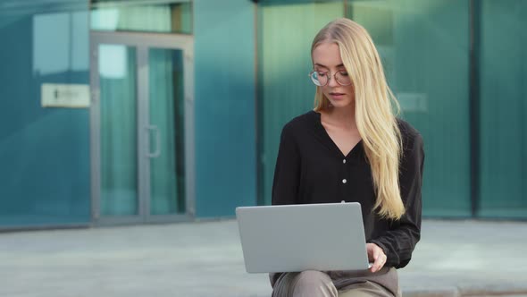 Pensive Millennial Woman in Glasses Look at Laptop Screen Outdoor Watching Online Conference or