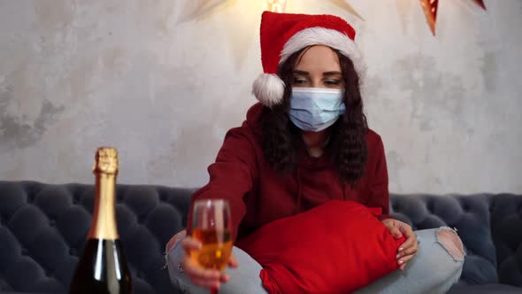 Young Woman in Medical Mask and Santa Claus Hat Offers Toast Looking at Camera